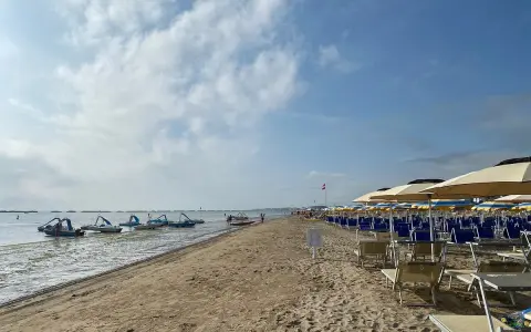 Pedalò in acqua e file di lettini e ombrelloni su una spiaggia sabbiosa, tipica di un bagno Roma di Levante.