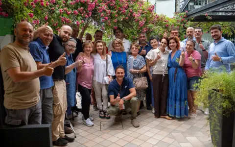 Un gruppo di persone sorridenti festeggia la primavera viserba sotto un pergolato fiorito.