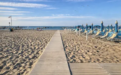 Passerella in legno sulla sabbia dorata di Rimini, con file di lettini e ombrelloni blu pronti per accogliere i bagnanti.