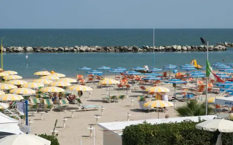 Spiaggia affollata con ombrelloni gialli e bianchi, lettini e il mare azzurro. Un'immagine di igea marittima, perfetta per una vacanza.