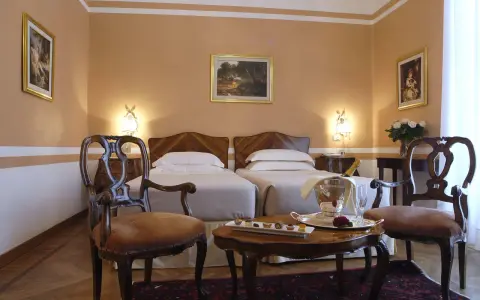 Camera elegante con due letti singoli, un tavolino con champagne e pasticcini, e sedie d'epoca. Un assaggio di lusso al Grand Hotel Rimini.