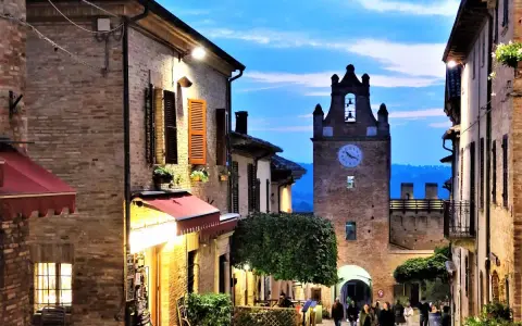 Borgo medievale illuminato al crepuscolo, con torre dell'orologio e vicoli suggestivi. Perfetto per scoprire cosa vedere vicino a Gradara.