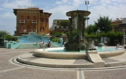 Fontana delle Sirene a Cattolica, con statue di sirene e tartarughe, circondata da edifici storici e una piazza acciottolata.
