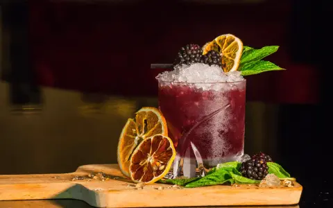 Cocktail rosso con frutti di bosco, arancia essiccata e menta, perfetto per un aperitivo a Riccione.