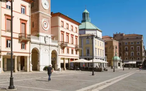 Passeggiata nella soleggiata piazza Tre Martiri a Rimini, con i suoi palazzi storici e il caratteristico orologio.