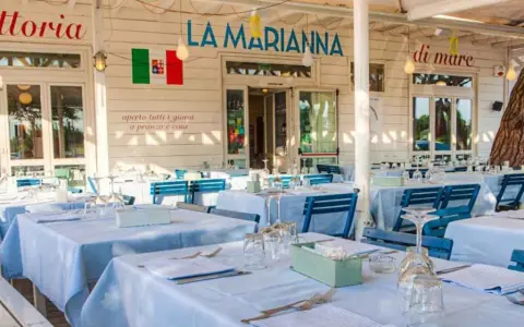 La Marianna Rimini, trattoria sul mare, con tavoli apparecchiati all'esterno sotto un grande albero.