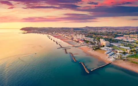 Alba rosata sul porto di Cattolica, con la costa e le spiagge dorate che si estendono verso l'orizzonte.