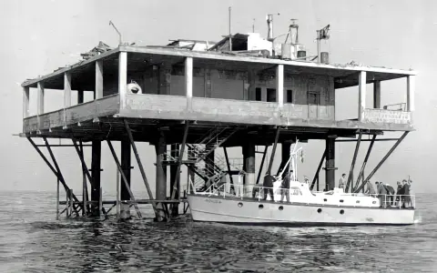 La struttura su palafitte, nota come Isola delle Rose, ospita persone su una barca ormeggiata.