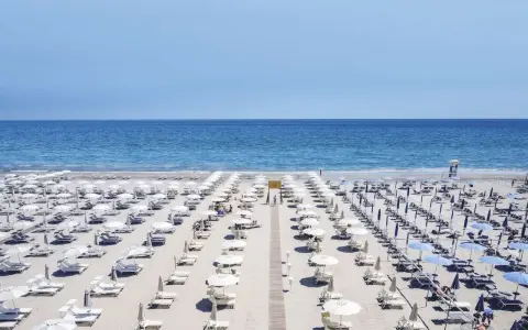 File di ombrelloni bianchi e lettini ordinati sui **stabilimenti balneari Cervia**, con il mare azzurro sullo sfondo.