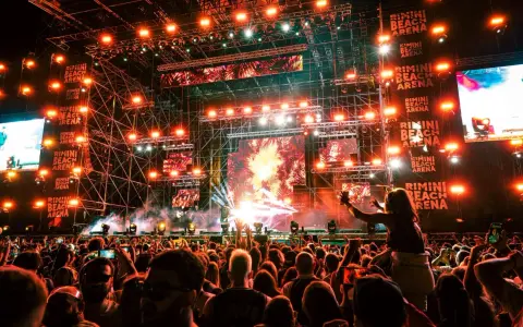 Folla in delirio al Rimini Beach Arena, luci psichedeliche e musica pulsante per un evento indimenticabile.