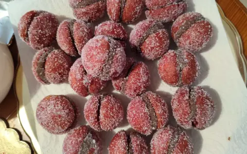 Dolci castagnole romagnole, due semisfere rosse unite da una crema scura e ricoperte di zucchero.