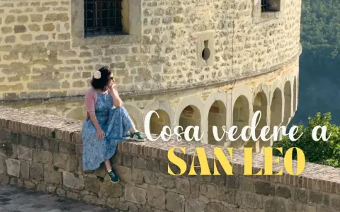 Donna seduta su un muretto di pietra, con vista panoramica. Un'ottima pausa durante il trekking a San Leo.