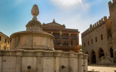 Fontana storica nel centro di Rimini, con edifici antichi sullo sfondo e cielo azzurro.