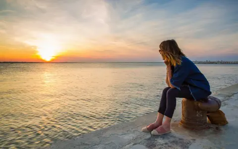 Donna seduta osserva il tramonto a Rimini, con il sole che si riflette sul mare calmo.
