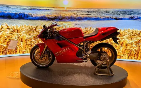 Ducati rossa su un palco, con sfondo di un campo di grano e il mare al tramonto. Un connubio perfetto tra la piada e il mare.