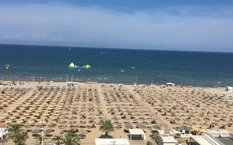 Una vasta spiaggia di Miramare gremita di ombrelloni e lettini, con bagnanti che si godono il sole e il mare azzurro.