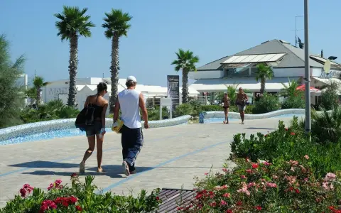 Coppia passeggia sul lungomare del parco mare nord Misano, tra palme e fiori.