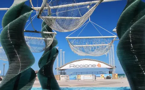 Sculture di vetro e reti sospese, con la scritta "Riccione" in lontananza. Un'idea di cosa vedere a Riccione, tra arte e mare.