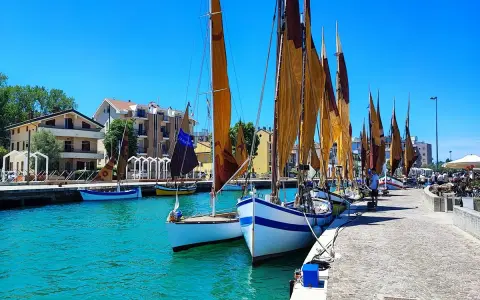 Barche a vela ormeggiate in un porto con case colorate sullo sfondo. Un dilemma: meglio Bellaria o Igea Marina?