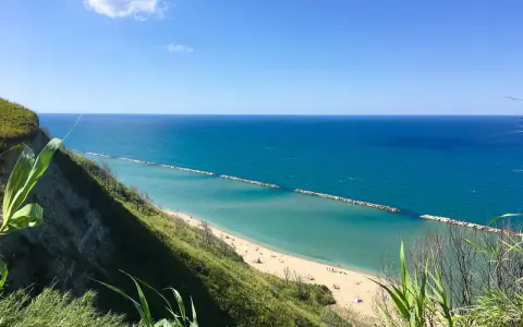Vista panoramica della spiaggia di Fiorenzuola di Focara, con mare azzurro e scogliera verdeggiante.