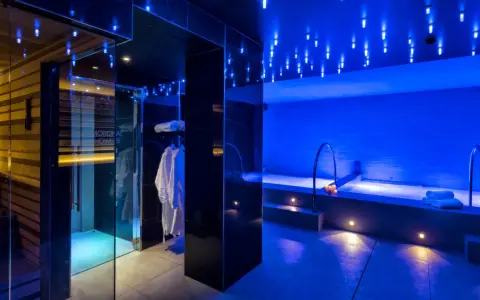 Interni di un centro benessere a Riccione con docce emozionali, vasca idromassaggio e accappatoi bianchi, illuminati da luci blu soffuse.
