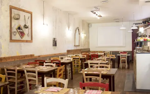 Interno di un ristorante accogliente, con tavoli apparecchiati e sedie colorate. Sembra proprio il posto ideale per una cena da "la mi mama Rimini".