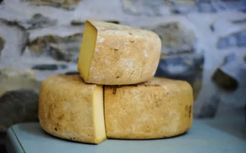 Formaggio Fossa stagionato, con crosta rustica e pasta gialla, impilato su uno sfondo di pietra grezza.