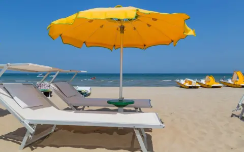 Spiagge di Rimini con lettini, ombrellone giallo e pedalò pronti per l'estate.