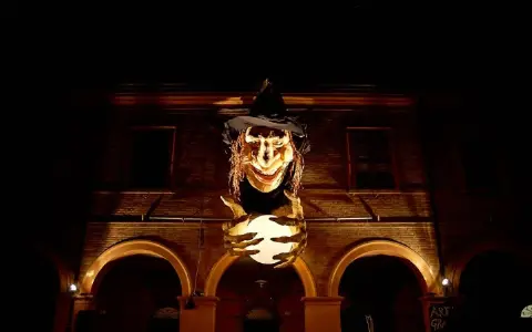 Una strega spaventosa con un cappello nero e una sfera luminosa in mano, illuminata nella notte. Sembra la protagonista de la notte delle streghe.