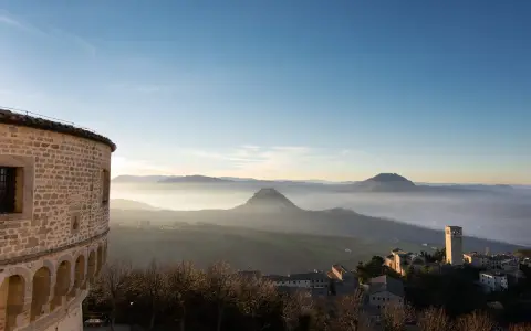 Panoramica di borghi vicino Riccione, con un antico torrione e colline nebbiose all'alba.