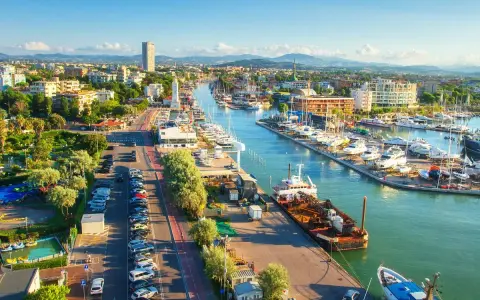 Vista aerea di un vivace **club nautico** con barche ormeggiate, edifici moderni e un faro bianco.