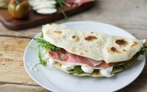 Piadina farcita con prosciutto crudo, mozzarella e rucola. Ecco come si farciscono le piadine per un pasto veloce e gustoso.