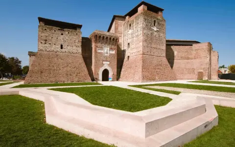 Imponente Castel Sismondo, con le sue torri in mattoni rossi e il cortile verdeggiante, si erge maestoso sotto un cielo azzurro.