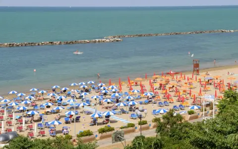 Spiaggia affollata con ombrelloni colorati, lettini e bagnanti. Perfetta idea per sapere dove andare al mare in Emilia Romagna.