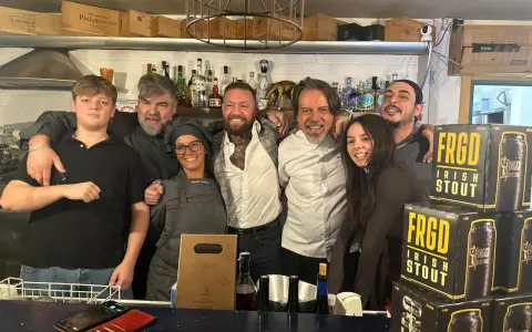 Staff sorridente a Misano Adriatico, con un ragazzo che sembra un gambero sbronzo tra loro. Sul bancone, bottiglie e lattine di "FRGD Irish Stout".