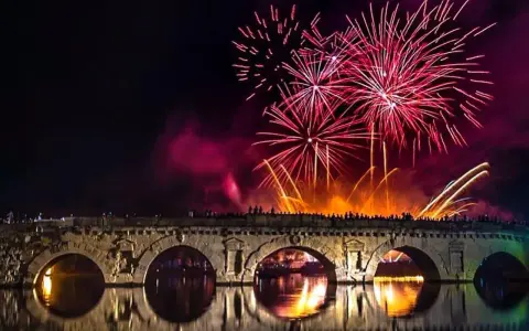 Fuochi d'artificio spettacolari illuminano il cielo notturno sopra un ponte storico, celebrando il capodanno in riviera romagnola.