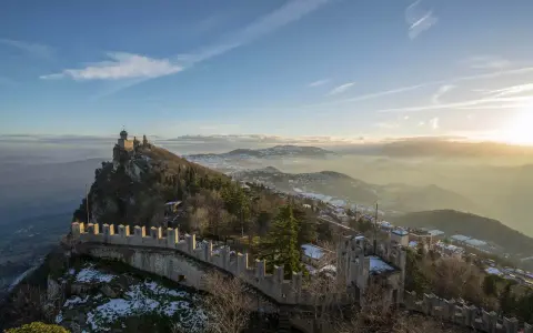 Un suggestivo viaggio a San Marino: torri medievali su un crinale roccioso, con la nebbia che avvolge le valli sottostanti al tramonto.