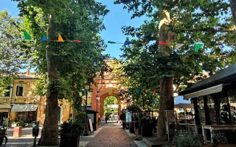 V Cervia centro, un viale alberato con festoni colorati conduce a un arco monumentale.