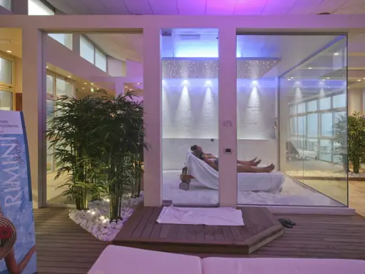 Un'oasi talassoterapico a Rimini, con due persone che si rilassano su lettini in un ambiente moderno e luminoso, circondato da piante di bambù e illuminazione soffusa.
