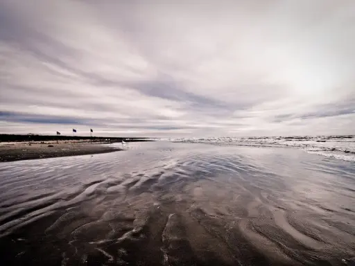 Spiaggia deserta con onde che lambiscono la riva, tre bandierine piantate nella sabbia bagnata. Un'atmosfera malinconica per questo mare d'inverno.
