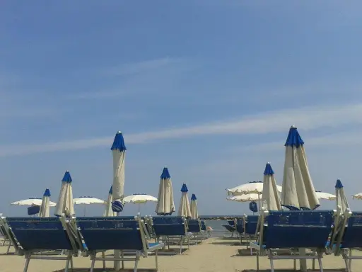 Spiaggia attrezzata al bar Lido di Savio, con lettini blu e ombrelloni bianchi e blu sotto un cielo limpido.