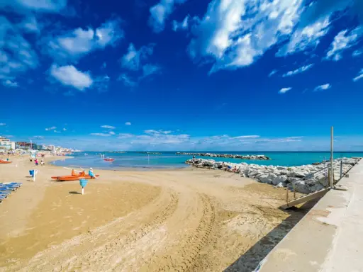 Spiaggia di Bellaria Mare con lettini, bagnini arancioni e mare azzurro sotto un cielo blu con nuvole bianche.
