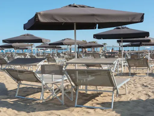 Lettini e ombrelloni scuri sulla sabbia dorata della **Baia degli Angeli Misano**, pronti per accogliere i bagnanti sotto il sole.