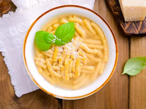 Piatto di passatelli in brodo, un classico dei piatti romagnoli, guarnito con basilico fresco e parmigiano.