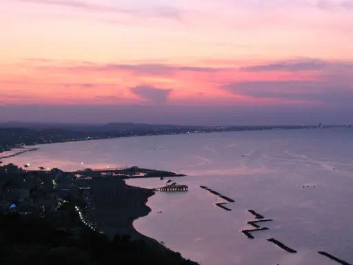 Panoramica Gabicce al tramonto, con cielo rosa e viola, mare calmo e costa illuminata.