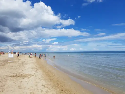 Una giornata di sole a Riccione mare, con gente che passeggia sulla sabbia e si gode l'acqua cristallina sotto un cielo azzurro con nuvole bianche.