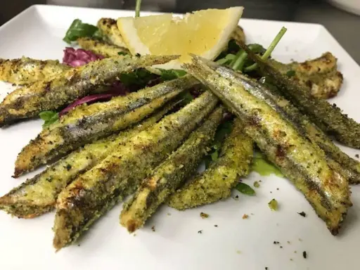 Sardoncini alla romagnola dorati e croccanti, serviti su un letto di insalata fresca con una fetta di limone.