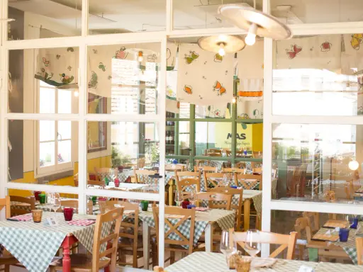 Interno di un'osteria de borg con tavoli apparecchiati con tovaglie a quadretti verdi e bianchi, sedie in legno e decorazioni colorate.