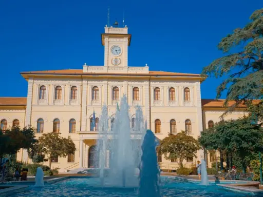 Fontana zampillante nella piazza Roosevelt di Cattolica, con un edificio giallo e un cielo azzurro.