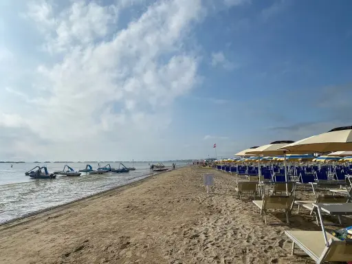 Pedalò in acqua e file di lettini e ombrelloni su una spiaggia sabbiosa, tipica di un bagno Roma di Levante.